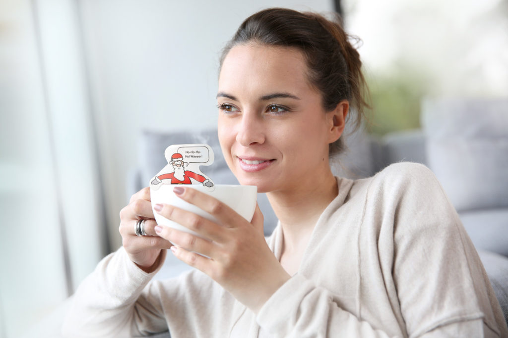 frau-mit-teefigur-in-teetasse Frau hält eine Tasse mit einer Usables Teefigur darin und schaut aus dem Fenster.
